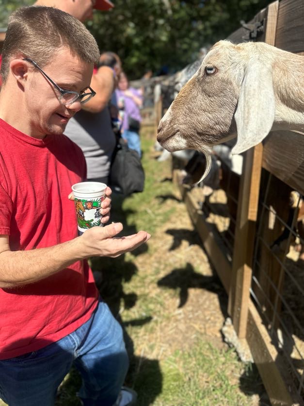 A man feeding a goat from his hand beside a wooden fence