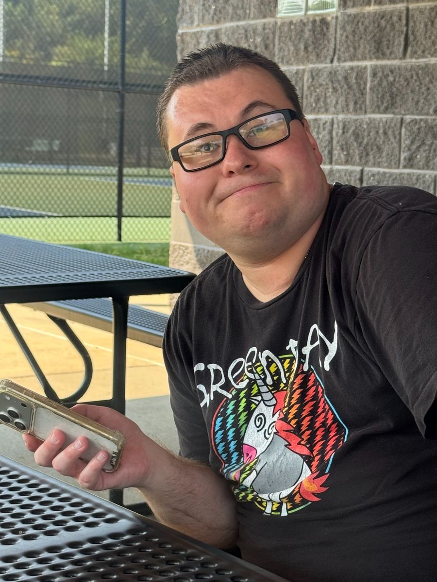 A young man wearing glasses smiling beside an outdoor picnic table