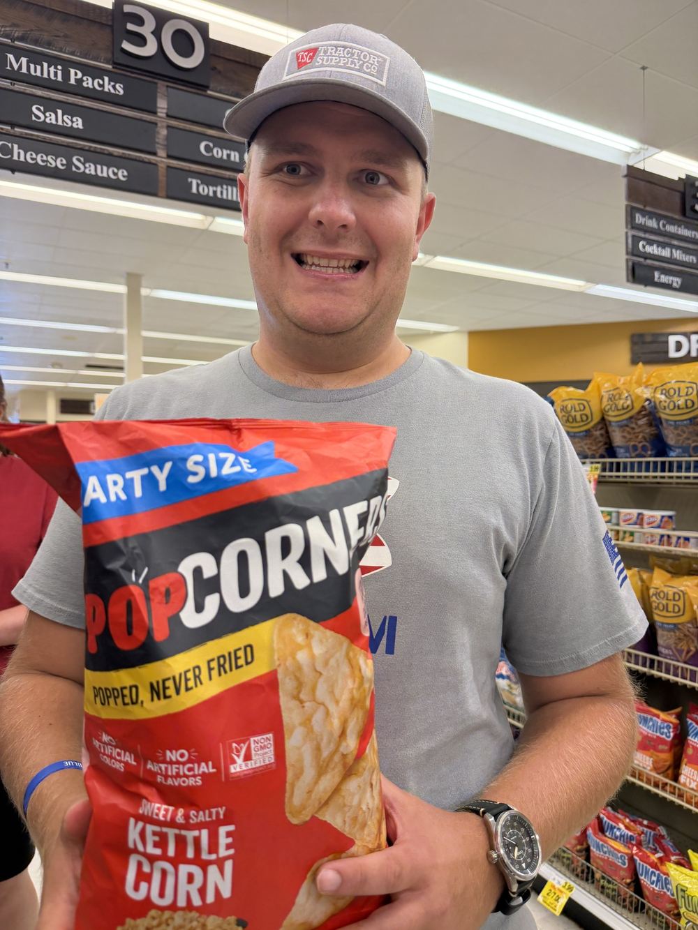A smiling man holding a bag of snacks in a grocery aisle