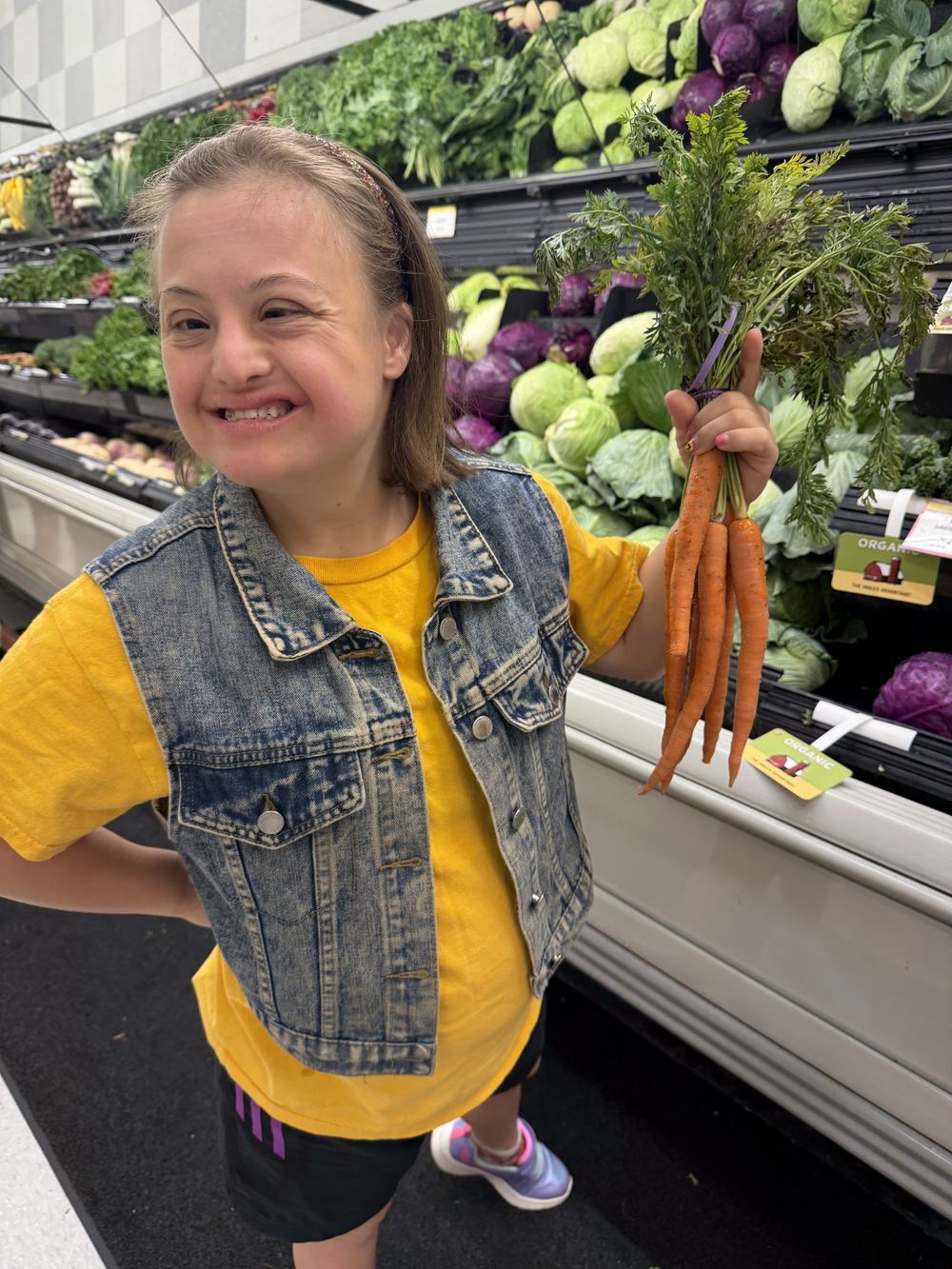 A smiling woman holding a bunch of carrots in a grocery store