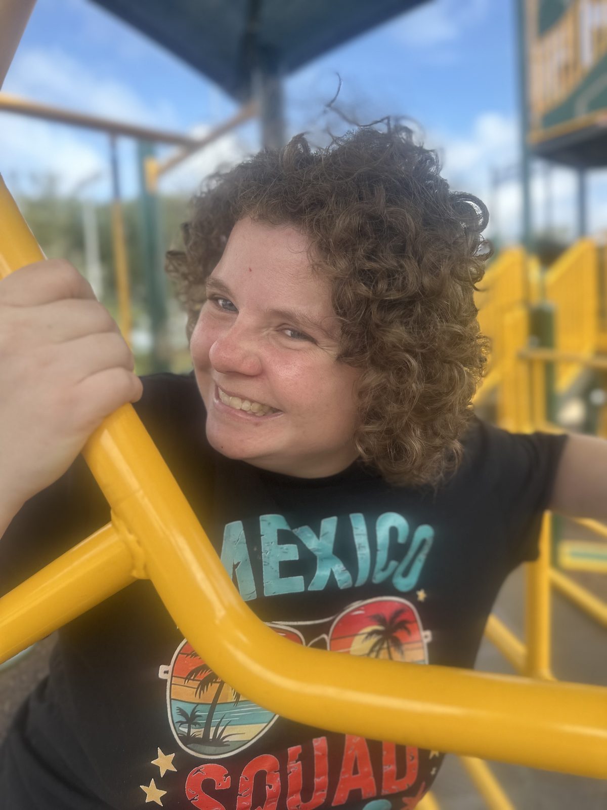 A smiling woman with her arms outstretched at an outdoor recreation area