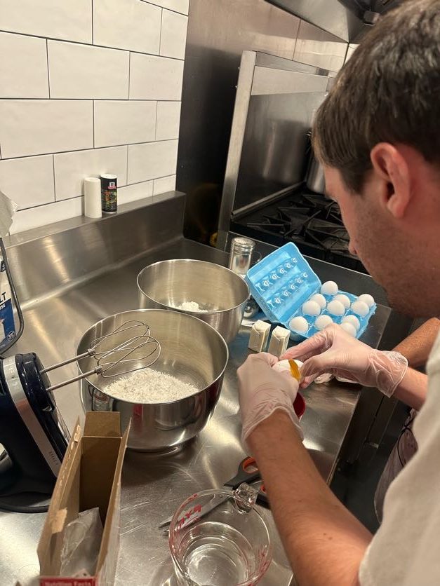 A person cracking an egg beside mixing bowls in a kitchen