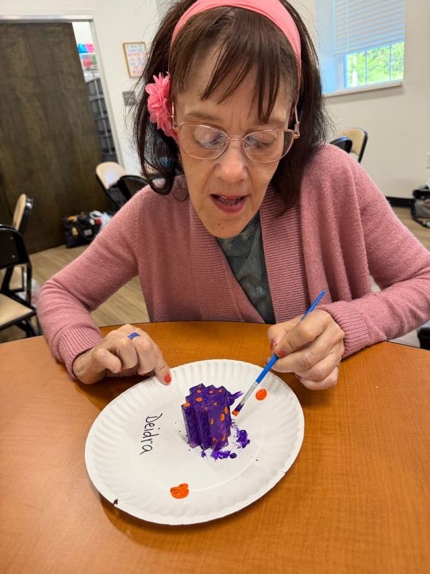 A woman using a paintbrush to decorate a small project at a table