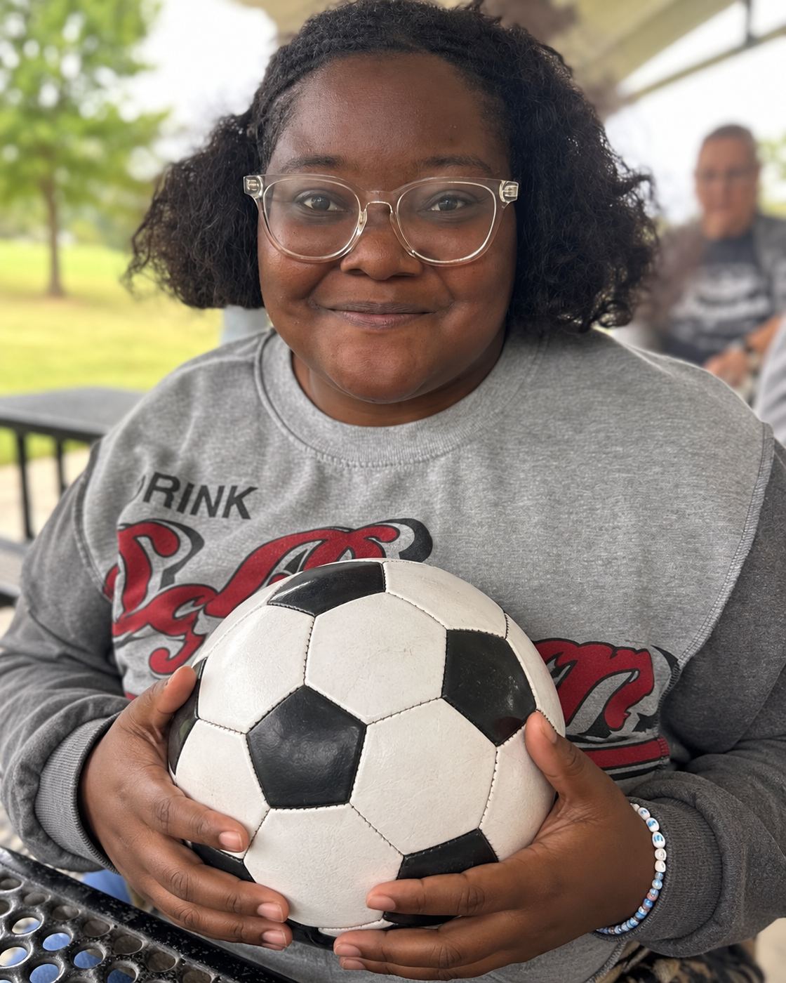 A smiling woman wearing glasses and holding a soccer ball